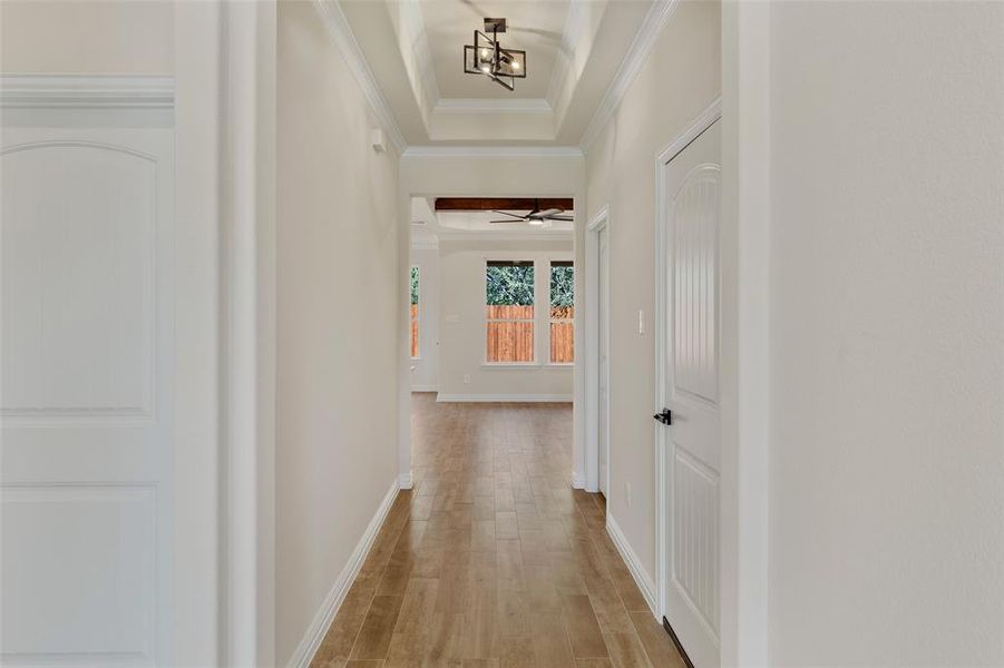 Hall with a tray ceiling, ornamental molding, a chandelier, and light hardwood / wood-style floors