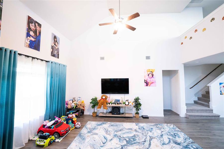 Spacious living area featuring vaulted ceilings, a ceiling fan with integrated lighting, and wood-finish flooring Spacious living area featuring vaulted ceilings, a ceiling fan with integrated lighting, and wood-finish flooring