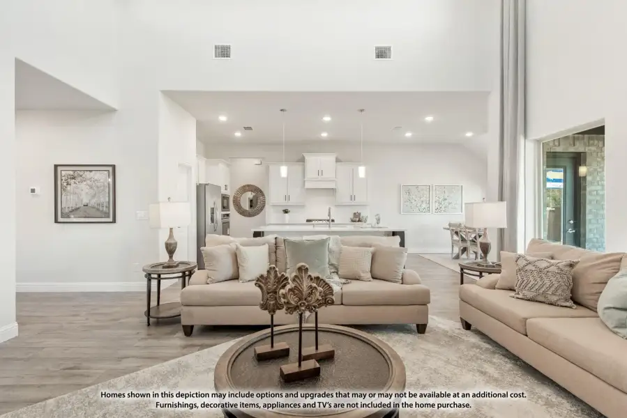 Open-concept living room with high ceilings and neutral sofas, open to white kitchen with island and pendant lights.