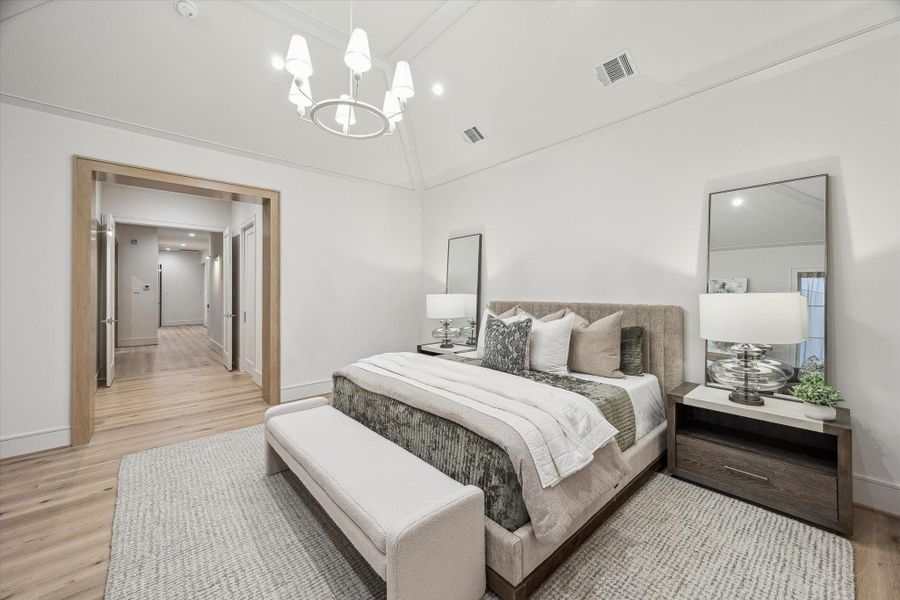 The primary suite features a vestibule entry with the spa-like bathroom to the right. The chandelier brings light and design interest to the room, which features a vaulted 12-foot ceiling.