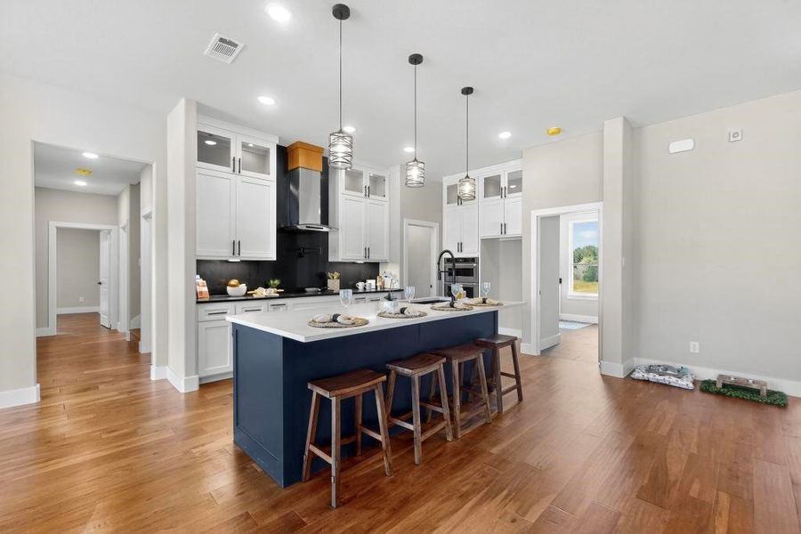 Kitchen featuring wall chimney exhaust hood, a kitchen island with sink, white cabinetry, decorative backsplash, and recessed lighting