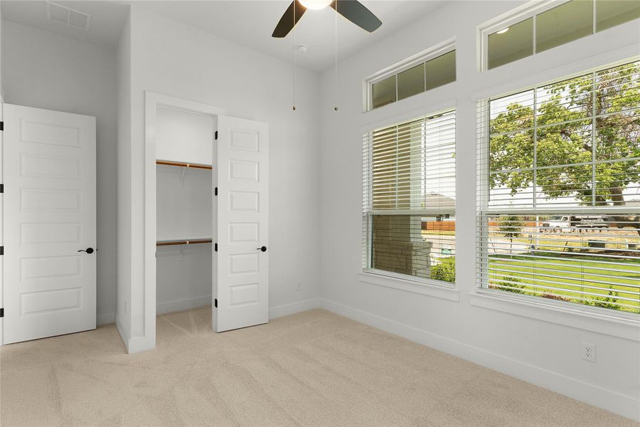 Unfurnished bedroom featuring carpet flooring, multiple windows, a spacious closet, and a ceiling fan Unfurnished bedroom featuring carpet flooring, multiple windows, a spacious closet, and a ceiling fan
