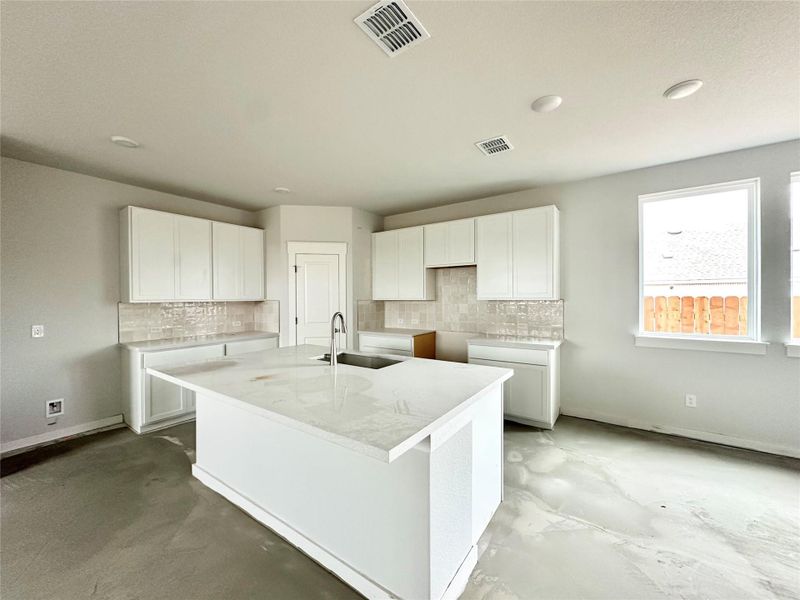 Kitchen with an island with sink, white cabinets, decorative backsplash, and light stone counters