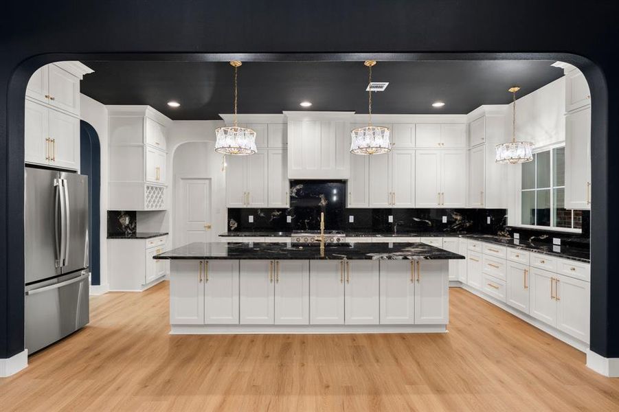 Kitchen with arched walkways, tasteful backsplash, freestanding refrigerator, a center island with sink, and hanging light fixtures