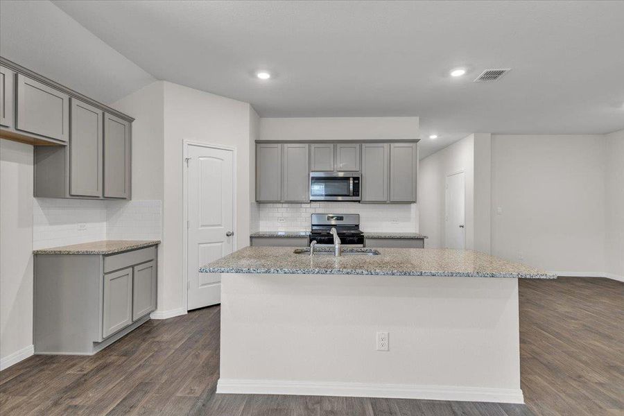 The kitchen features gray cabinetry, a kitchen island with a sink, a microwave, and a stove