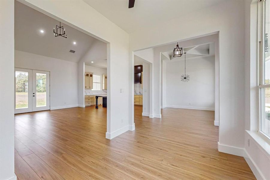 Unfurnished living room with vaulted ceiling, french doors, and light wood-type flooring