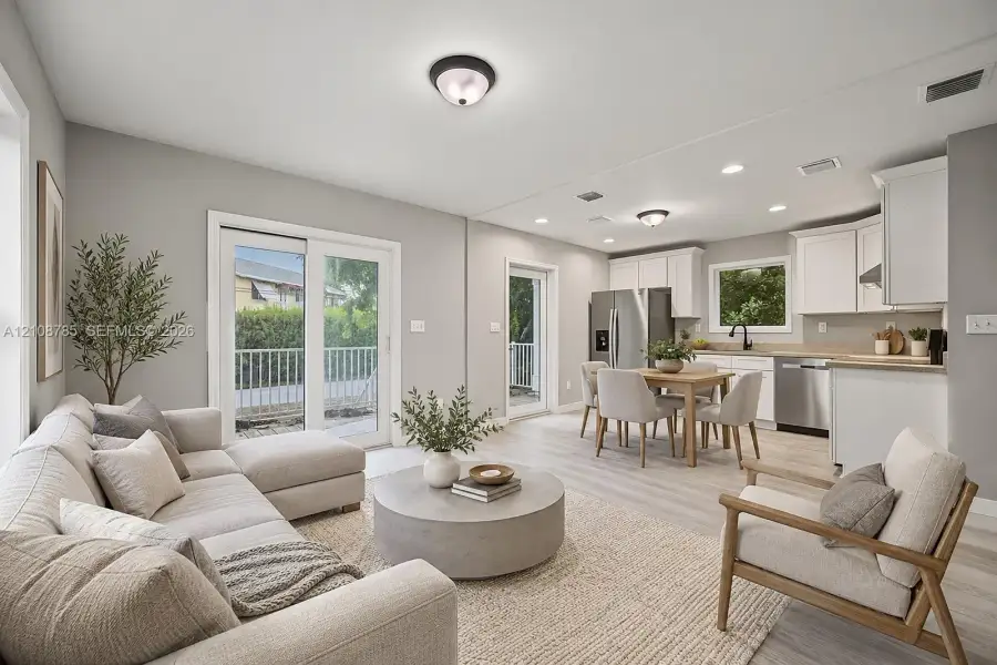 Open-concept living space featuring wood-finish flooring, white cabinetry, stainless steel appliances, recessed lighting, and glass sliding doors Open-concept living space featuring wood-finish flooring, white cabinetry, stainless steel appliances, recessed lighting, and glass sliding doors