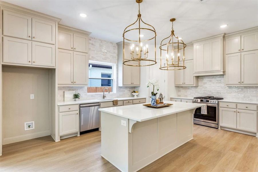 Kitchen featuring cream cabinets, stainless steel appliances, pendant lighting, backsplash, and light wood-style flooring Kitchen featuring cream cabinets, stainless steel appliances, pendant lighting, backsplash, and light wood-style flooring