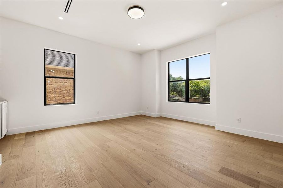 Spacious room featuring light wood-finish flooring, white walls, and recessed lighting