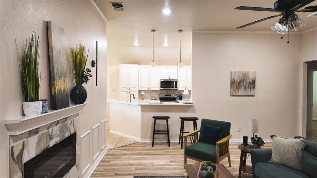 Open concept living area featuring wood-finish flooring, a contemporary fireplace with a decorative mantel, and crown molding