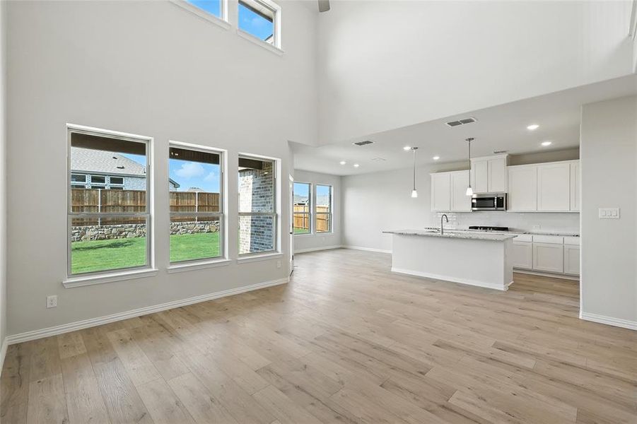 Unfurnished living room featuring light wood-style floors and a high ceiling Unfurnished living room featuring light wood-style floors and a high ceiling