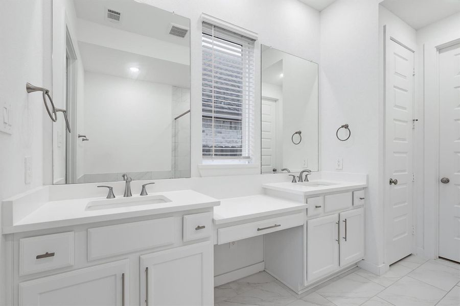 The luxurious primary bathroom also boasts two sink vanities with a built in vanity desk, and striking tile flooring, offering both elegance and convenience in a spa like setting.