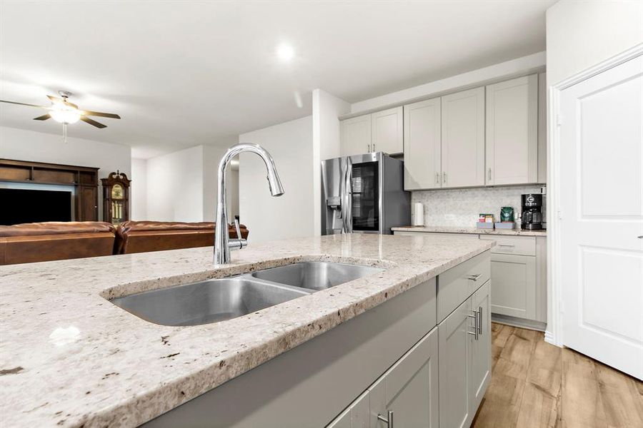 Kitchen featuring stainless steel refrigerator with ice dispenser, tasteful backsplash, light stone counters, a ceiling fan, and light wood-style flooring Kitchen featuring stainless steel refrigerator with ice dispenser, tasteful backsplash, light stone counters, a ceiling fan, and light wood-style flooring