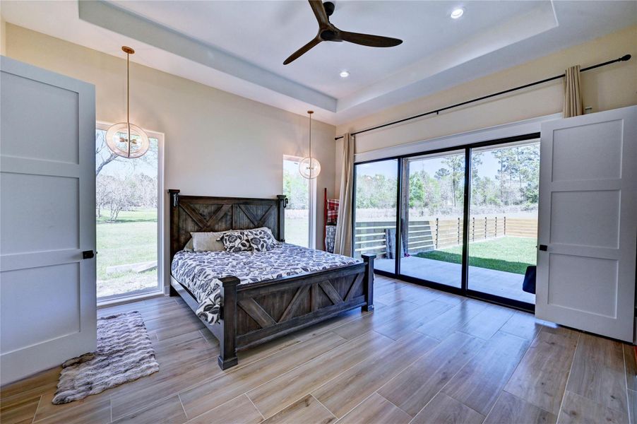 This spacious bedroom features modern pendant lighting, and large sliding glass doors that open to a serene outdoor view, creating a bright and inviting atmosphere.