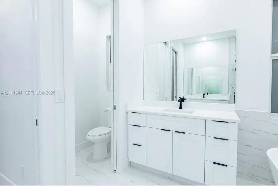White vanity with shaker-style cabinetry, quartz countertop, matte black hardware, integrated sink, and large wall-mounted mirror White vanity with shaker-style cabinetry, quartz countertop, matte black hardware, integrated sink, and large wall-mounted mirror