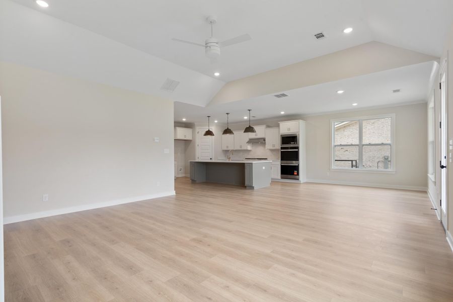 Vaulted ceilings with recessed lighting, wood-finish flooring, and a kitchen featuring a center island, white cabinetry, and built-in double ovens Vaulted ceilings with recessed lighting, wood-finish flooring, and a kitchen featuring a center island, white cabinetry, and built-in double ovens