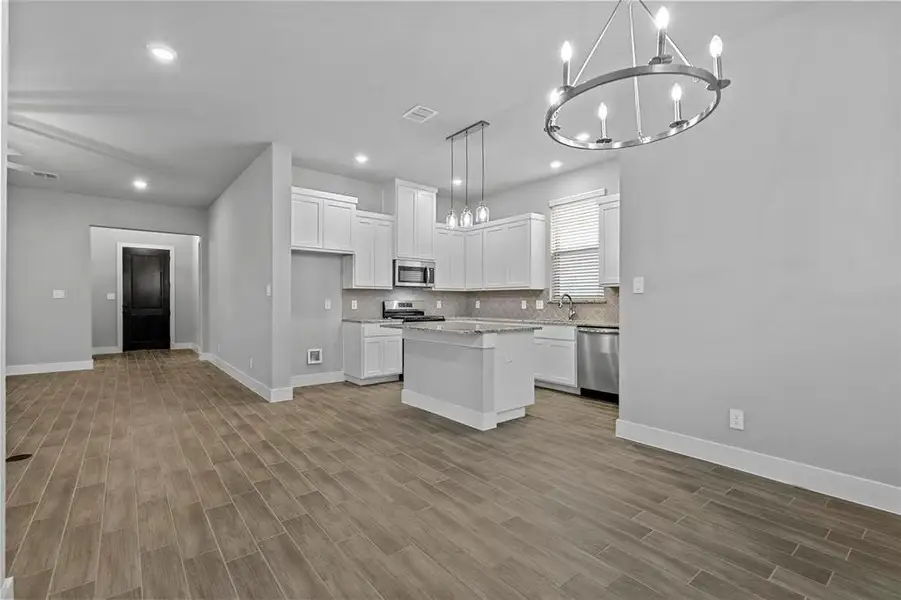 Kitchen with appliances with stainless steel finishes, light hardwood / wood-style flooring, a center island, white cabinets, and pendant lighting