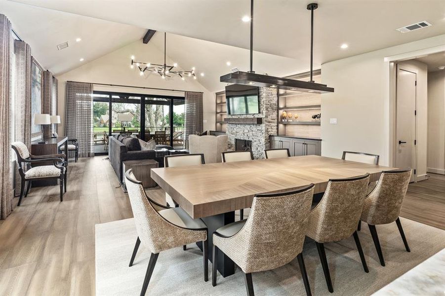 Dining space with a fireplace, light hardwood / wood-style floors, a notable chandelier, and beam ceiling