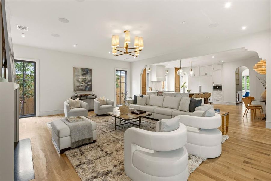 Spacious living area featuring light wood-finish flooring, recessed lighting, and a prominent chandelier Spacious living area featuring light wood-finish flooring, recessed lighting, and a prominent chandelier