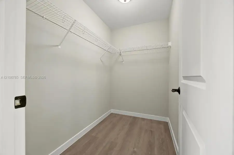 Walk-in closet featuring wood-finish flooring, white walls, and integrated wire shelving Walk-in closet featuring wood-finish flooring, white walls, and integrated wire shelving
