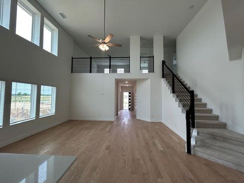 Unfurnished living room with visible vents, a towering ceiling, light wood-style floors, baseboards, and stairway