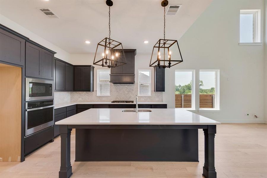Kitchen featuring backsplash, an island with sink, pendant lighting, light wood-style flooring, and stainless steel appliances Kitchen featuring backsplash, an island with sink, pendant lighting, light wood-style flooring, and stainless steel appliances