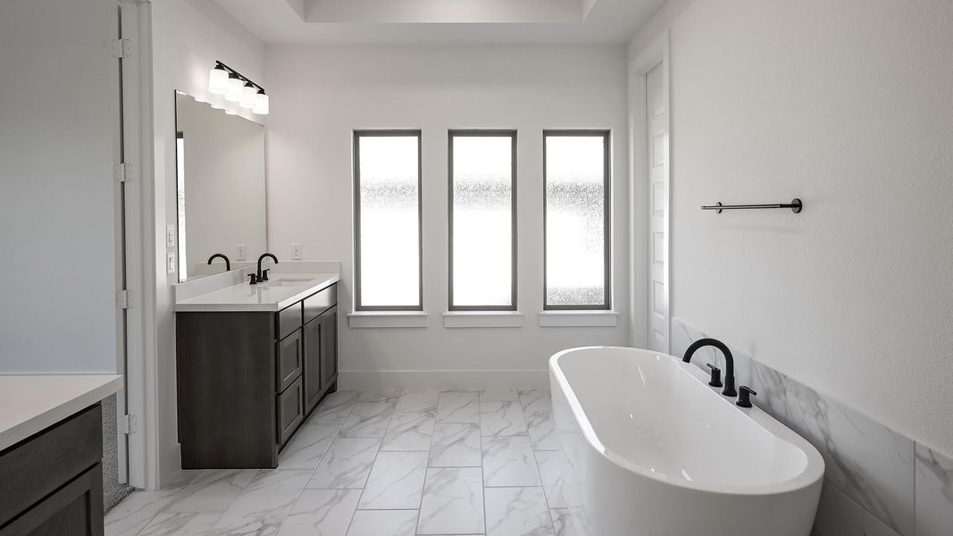 Bathroom with marble finish floor, a soaking tub, vanity, and baseboards