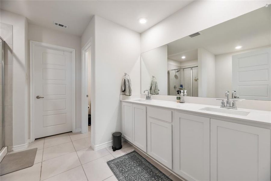 Bathroom featuring double vanity, a shower stall, and light tile patterned floors