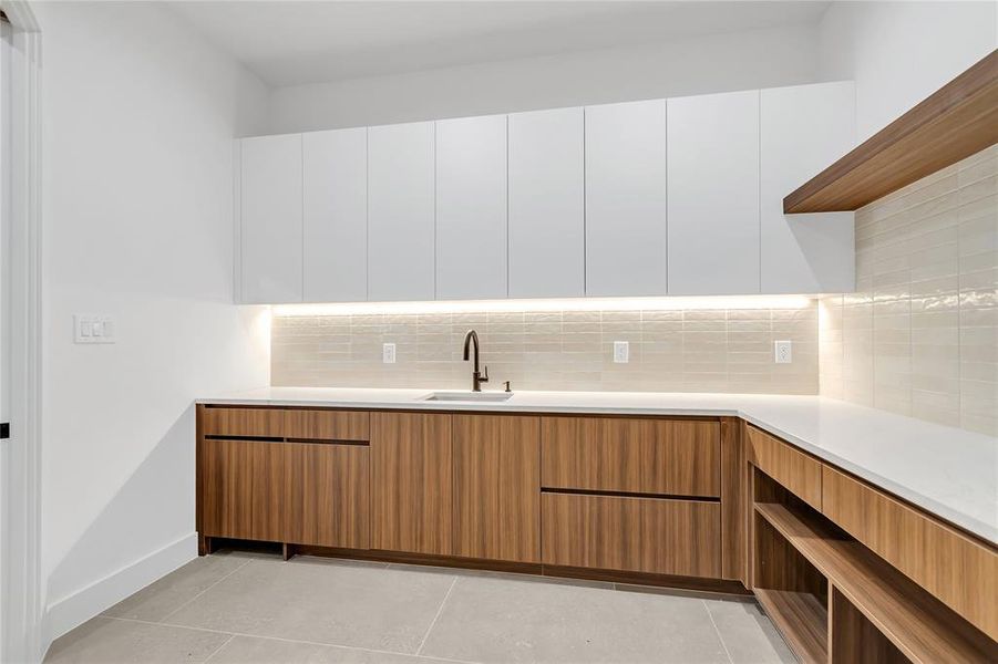 Kitchen featuring modern cabinets, light countertops, backsplash, and white cabinets Kitchen featuring modern cabinets, light countertops, backsplash, and white cabinets