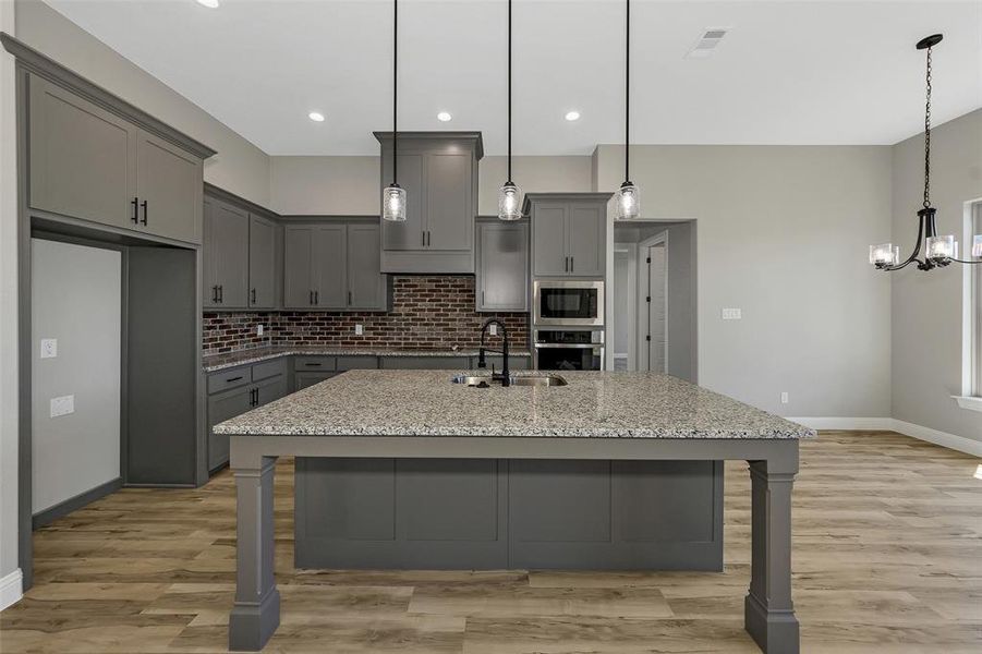 Kitchen with gray cabinets, decorative backsplash, a breakfast bar area, light stone counters, and a chandelier