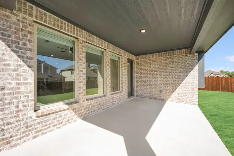 Covered back patio with concrete floor, brick exterior, sliding glass door, and fenced backyard with green lawn