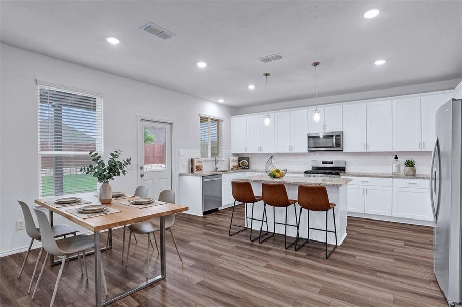 Spacious open-concept kitchen and dining area featuring wood-finish flooring, white cabinetry, a kitchen island with seating, a stainless steel appliance suite, and recessed lighting