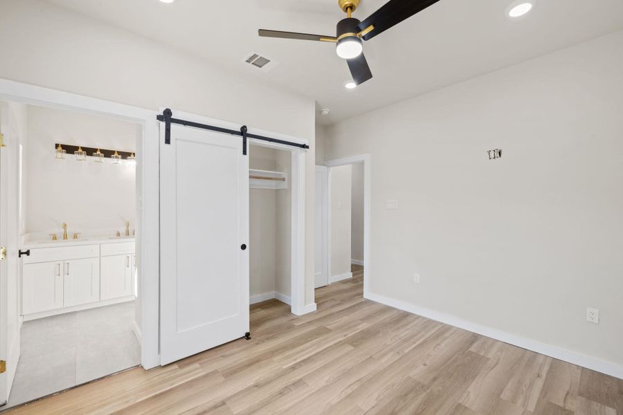 Unfurnished bedroom featuring a barn door, light wood finished floors, recessed lighting, a ceiling fan, and a closet Unfurnished bedroom featuring a barn door, light wood finished floors, recessed lighting, a ceiling fan, and a closet