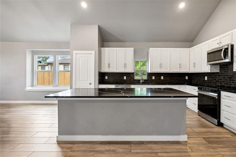 Kitchen with a center island, vaulted ceiling, stainless steel appliances, and white cabinets