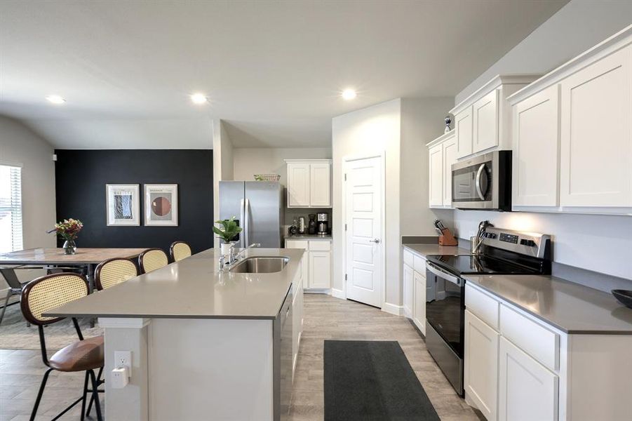 Kitchen featuring stainless steel appliances, a sink, an island with sink, and a kitchen bar