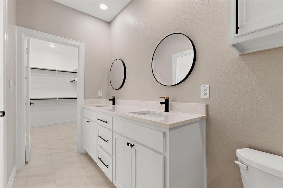 Bathroom with double vanity, a walk in closet, a textured wall, recessed lighting, and light tile patterned flooring Bathroom with double vanity, a walk in closet, a textured wall, recessed lighting, and light tile patterned flooring