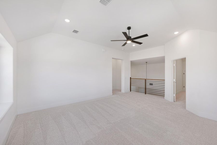 Spacious upstairs bonus room with vaulted ceiling, ceiling fan, carpet flooring, and open railing overlooking lower level.