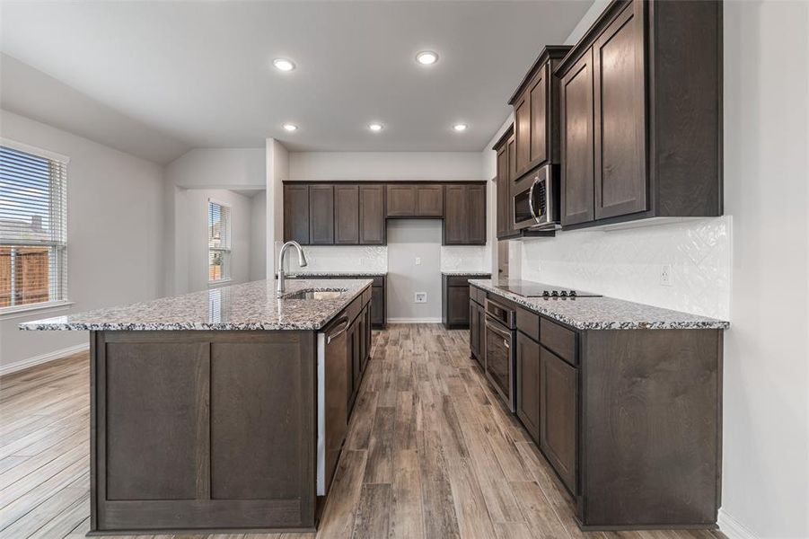 Kitchen with light stone counters, dark brown cabinetry, recessed lighting, backsplash, and appliances with stainless steel finishes Kitchen with light stone counters, dark brown cabinetry, recessed lighting, backsplash, and appliances with stainless steel finishes