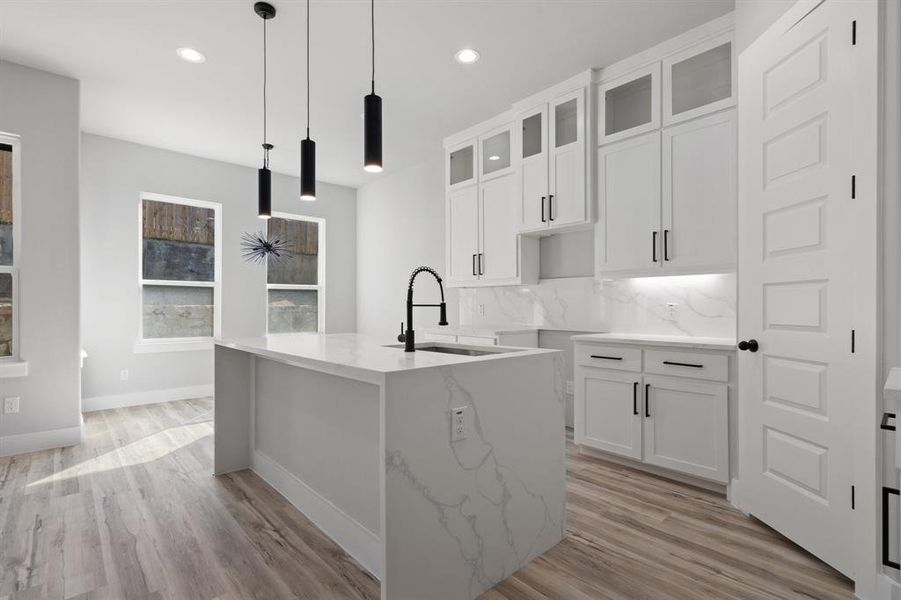 Kitchen with tasteful backsplash, an island with sink, sink, and decorative light fixtures