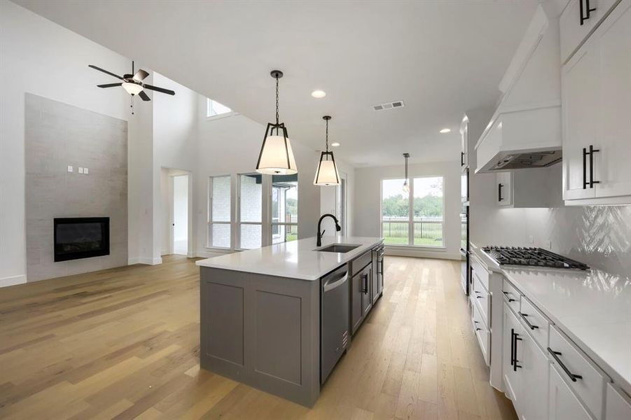 Open-concept living space featuring a central island kitchen, wood-finish flooring, and a fireplace with a textured surround Open-concept living space featuring a central island kitchen, wood-finish flooring, and a fireplace with a textured surround