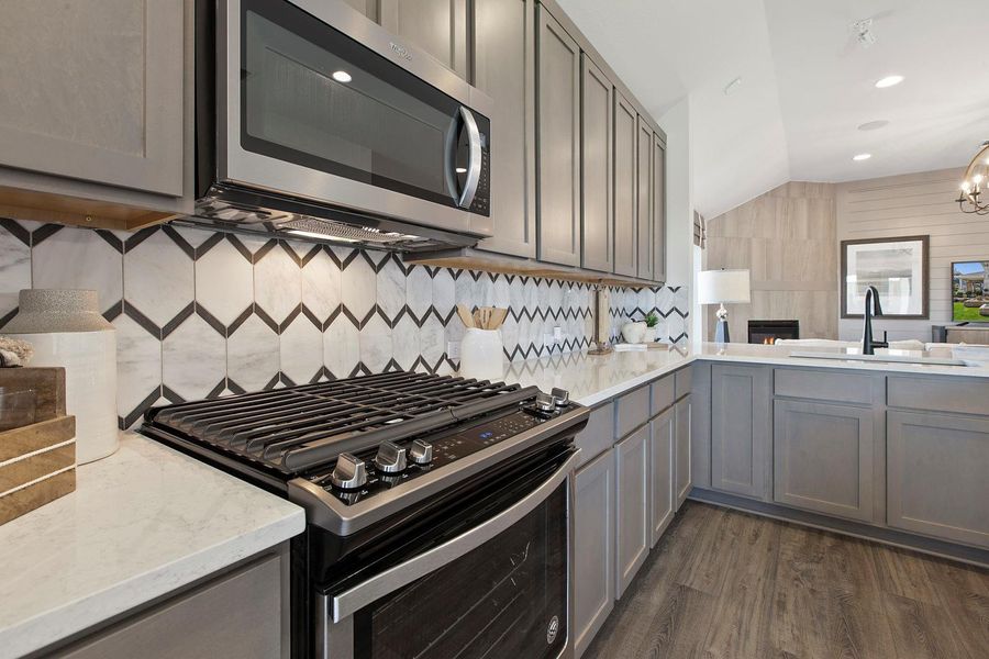 Kitchen featuring appliances with stainless steel finishes, vaulted ceiling, dark wood-style floors, gray cabinets, and light stone countertops Kitchen featuring appliances with stainless steel finishes, vaulted ceiling, dark wood-style floors, gray cabinets, and light stone countertops