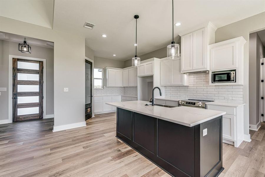 Kitchen with white cabinets, sink, a kitchen island with sink, decorative light fixtures, and stainless steel appliances