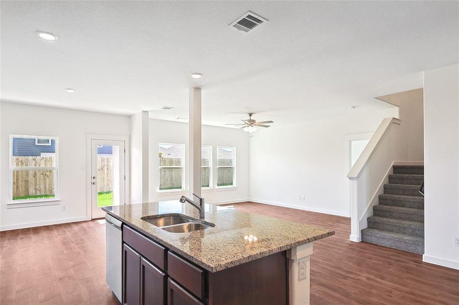 Kitchen with dark wood finish cabinetry, light stone counters, dark wood-type flooring, an island with sink, and dishwasher