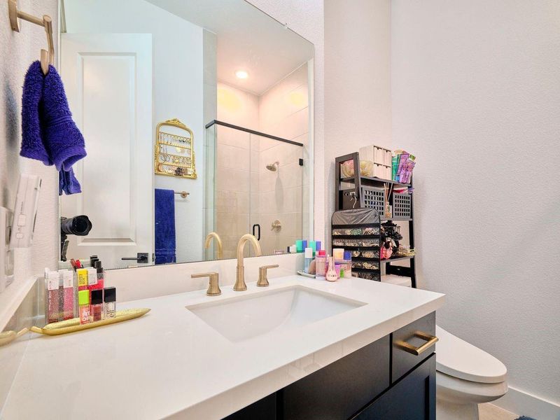 Experience luxury in the first-floor guest bedroom with an en-suite bath, featuring a sleek vanity with dual gold fixtures and a walk-in glass shower.