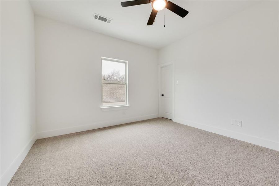 Carpeted spare room with baseboards, visible vents, and a ceiling fan