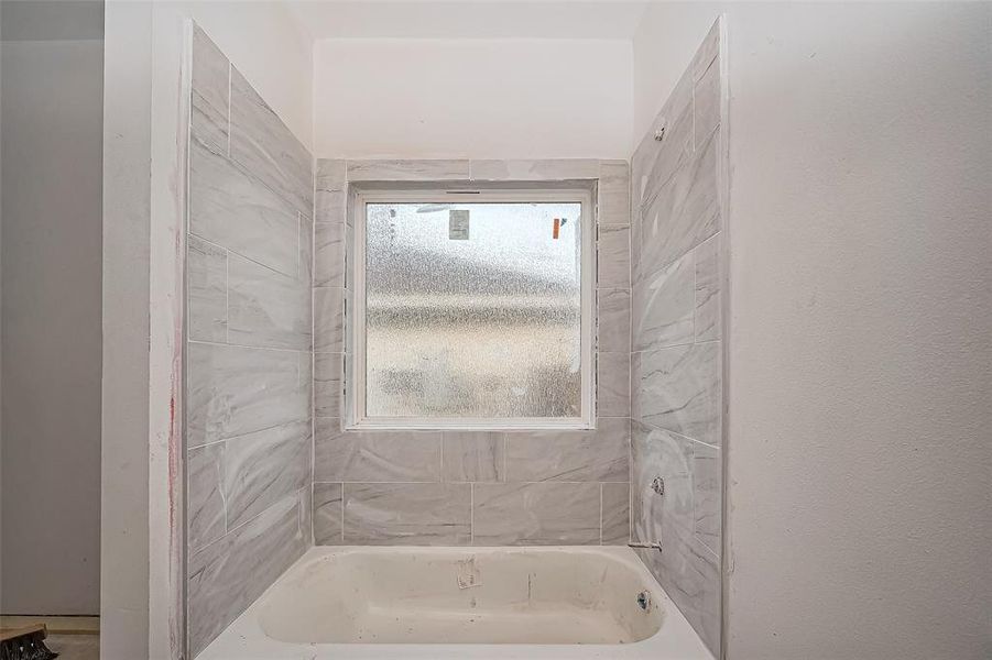 A shower-tub combo with tiled walls sits beside a frosted window, allowing for privacy without sacrificing light.