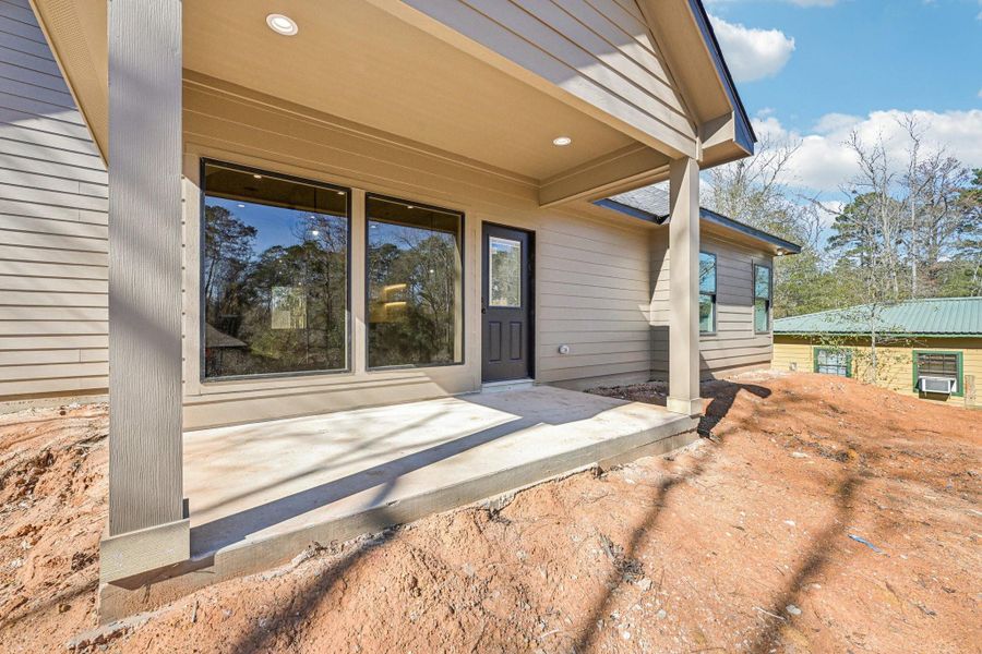 Back patio with large windows, a covered area, and a sturdy design. The patio overlooks a natural setting, offering a serene outdoor space.