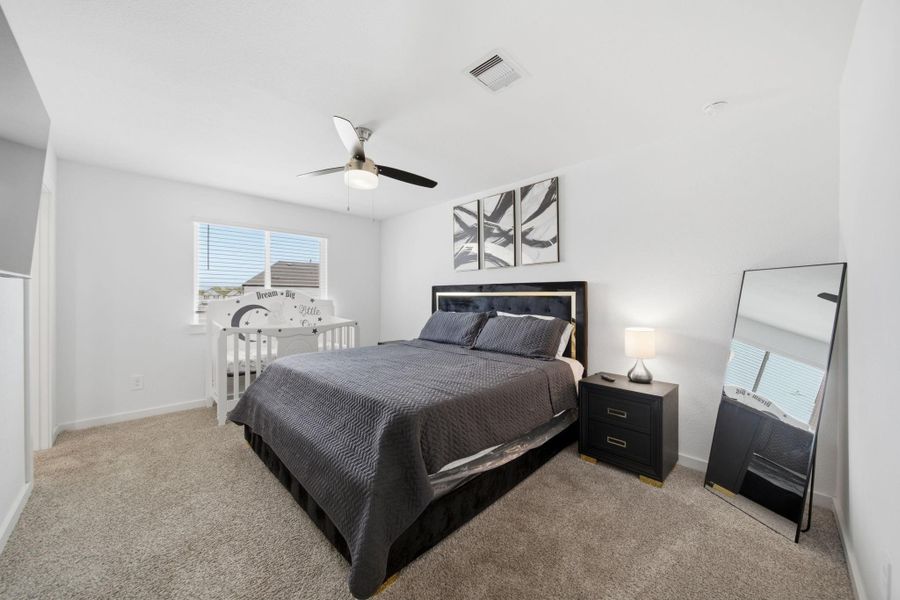 Spacious primary bedroom with neutral tone carpet and walls, bright natural lighting, and ceiling fan.