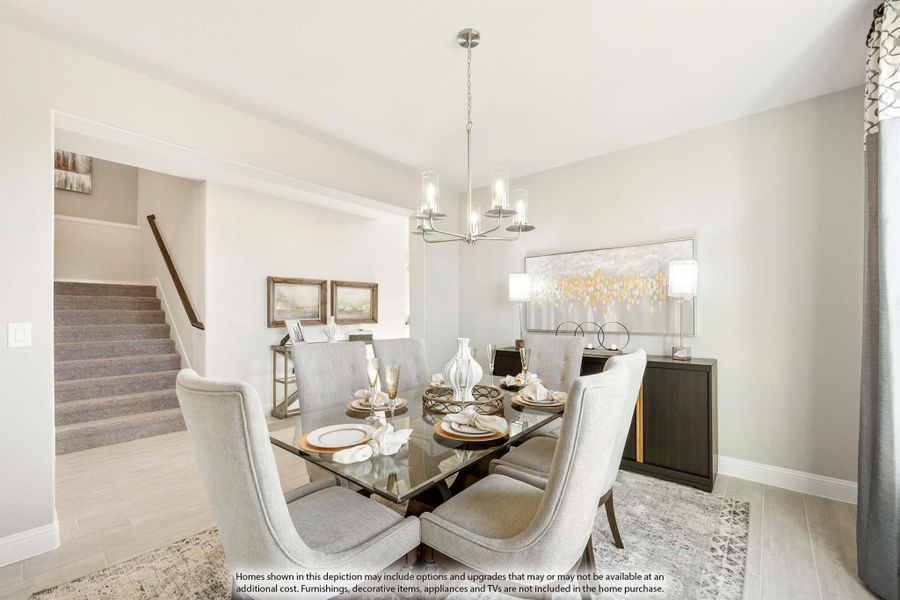 Dining room with glass-top table, gray upholstered chairs, chandelier, and staircase visible in background