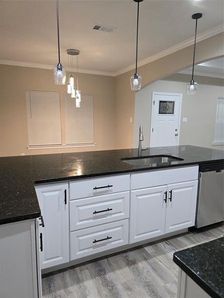 Kitchen featuring dishwashing machine, white cabinetry, sink, and decorative light fixtures